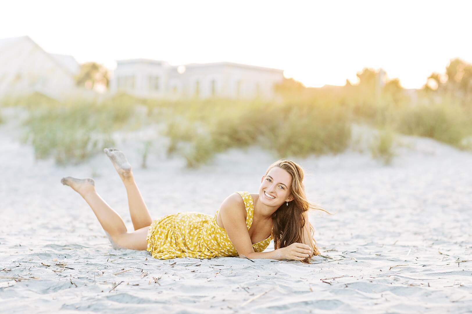 Casual Beach Pictures of High School Senior in yellow dress laying on sand