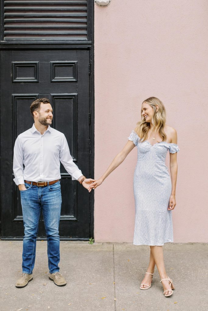 Symmetrical photo of guy in front of black door and girl by pink wall holding hands 